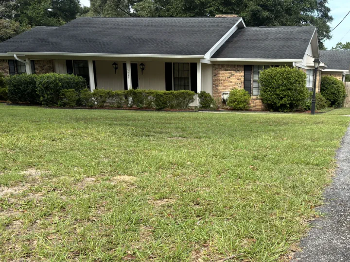 The same front lawn after mowing — grass cut short and even from the curb up to the house, the brick ranch and driveway behind under a brighter sky